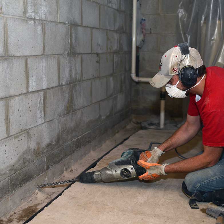 Man drilling weep holes during a basement repair job